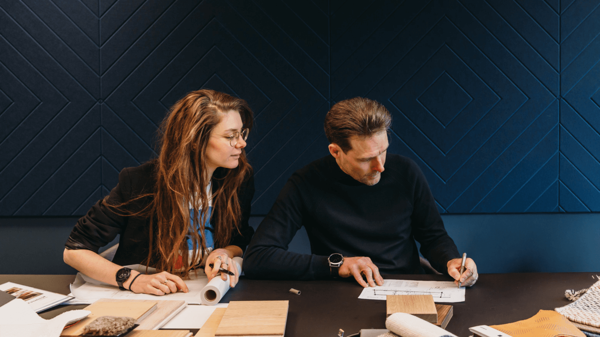 man en vrouw samen aan het werk met materialen en stofstalen op een tafel